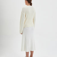 Feminine wool sweater in cream with scalloped accents on neckline, waist, and cuffs.
