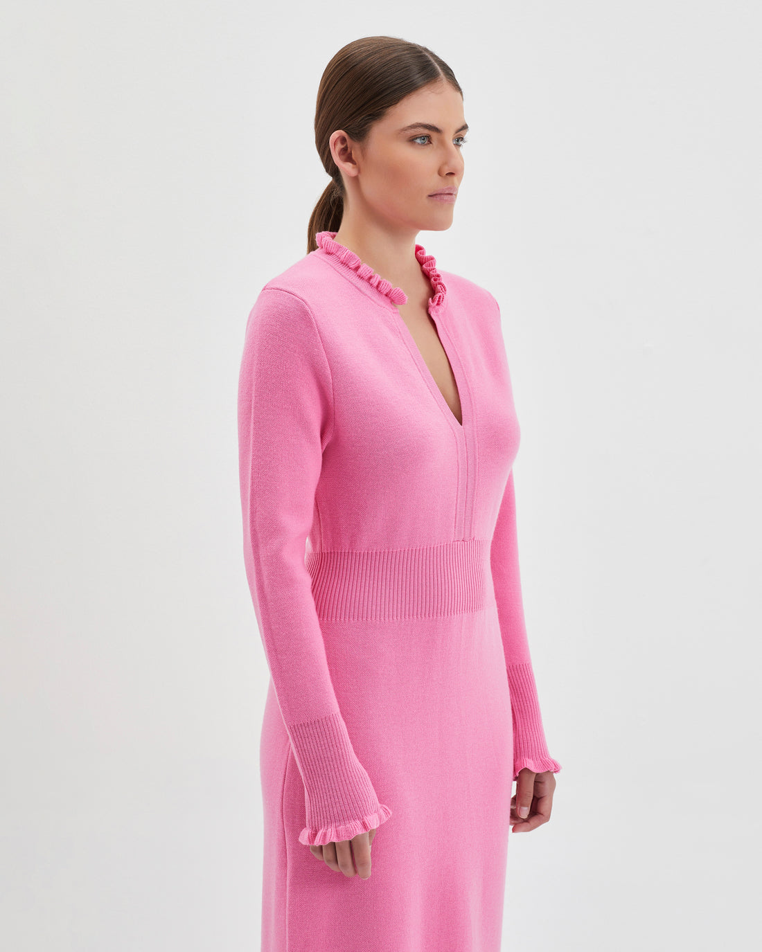 The dress showcases a flattering deep V-neckline framed by a delicate ruffled trim for a feminine touch